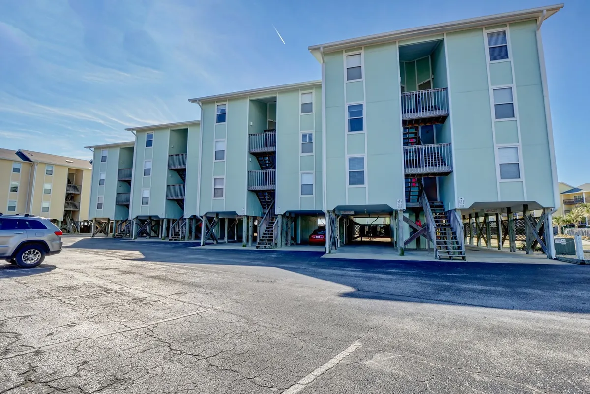An exterior perspective of the Surf Condos buildings, featuring a three-story structure with staircases and a surrounding parking lot. The setting suggests a communal, accessible atmosphere, suitable for gatherings, barbecues, and family activities mentioned in the section.