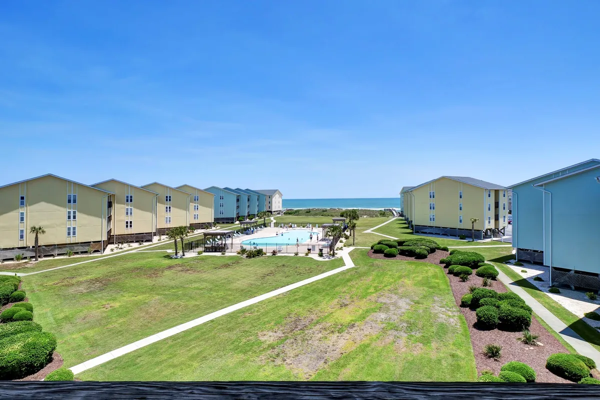 A sunny exterior shot of the Surf Condos’ pool area, showing a sparkling swimming pool surrounded by a well-kept green lawn. The pool is framed by lounge chairs, palm trees, and glimpses of the adjacent beach and condominium buildings, creating a lively and inviting social environment.