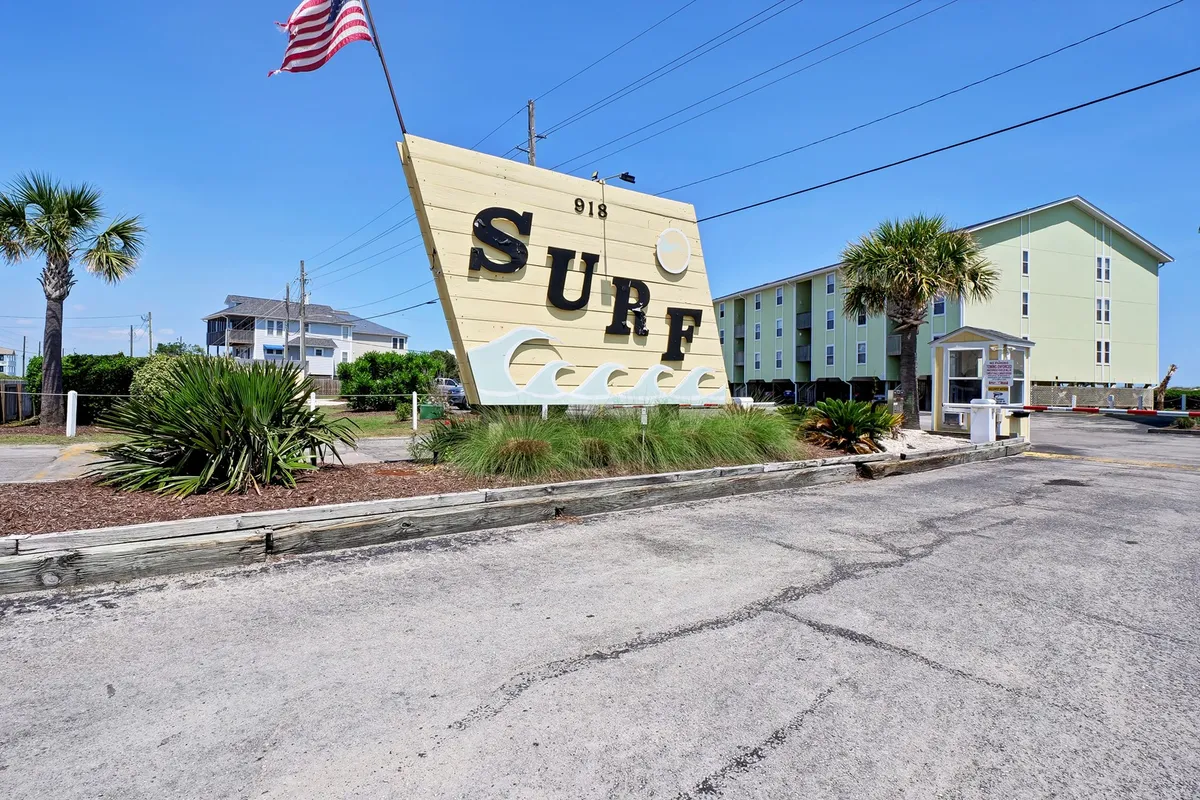 An inviting exterior shot featuring a large 'SURF' sign, surrounded by palm trees and neighboring buildings. The vibrant scene captures the sunny, cheerful essence of Surf City, suggesting proximity to the beach and the lively atmosphere of local attractions.